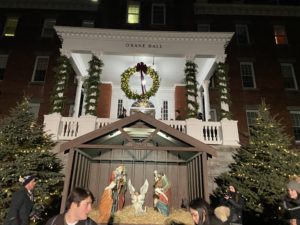 A Nativity scene sandwiched in between two lit-up Christmas trees in front of O’Kane Hall, which is also decorated with Christmas greenery.